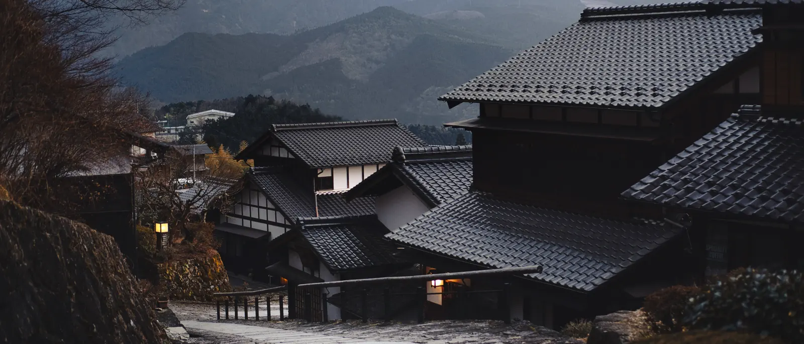 A stone-paved street curving between deep-eaved timber inns below snow-streaked mountains at dusk